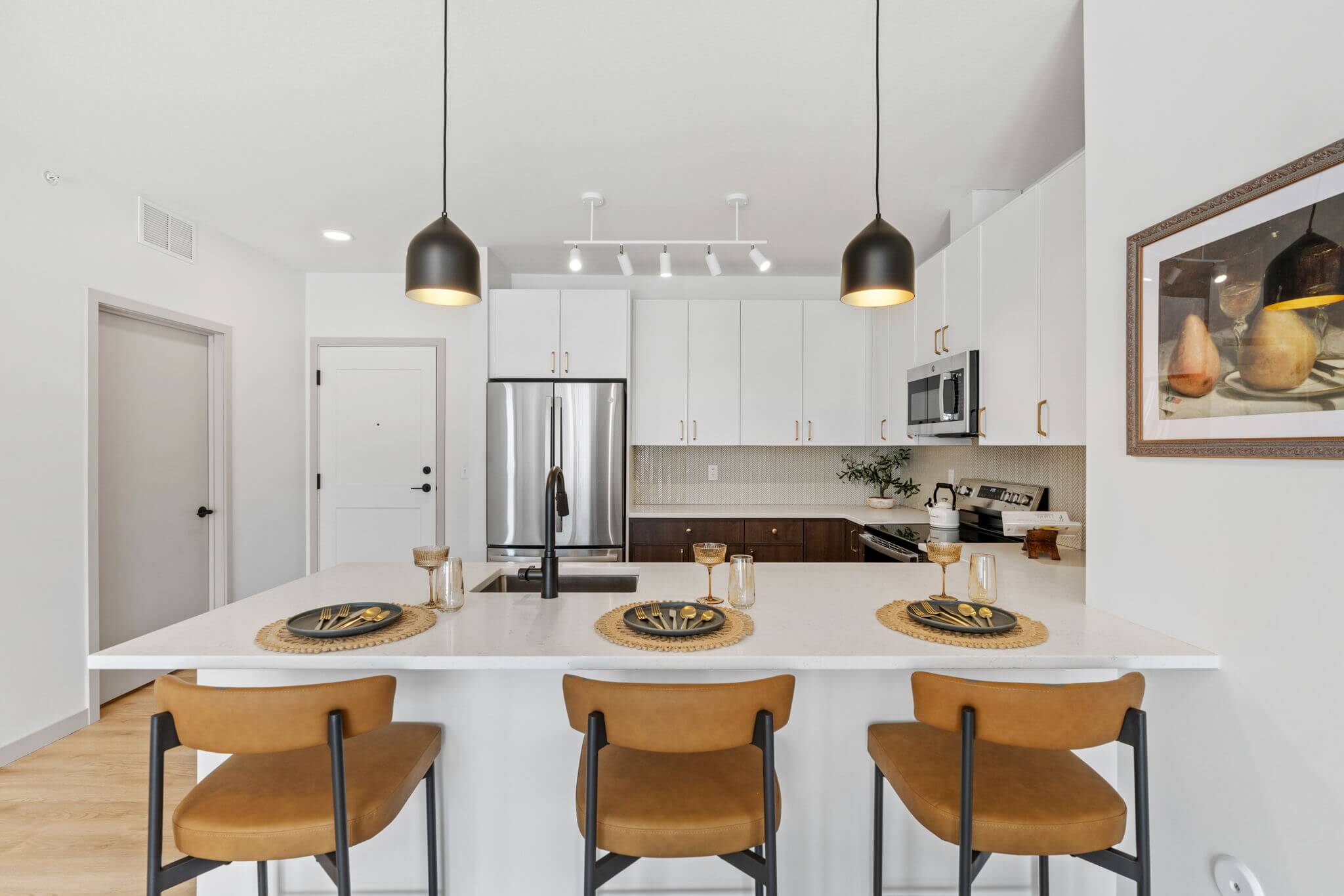 Kitchen view with three pendant lights above island and warm-toned bar stools