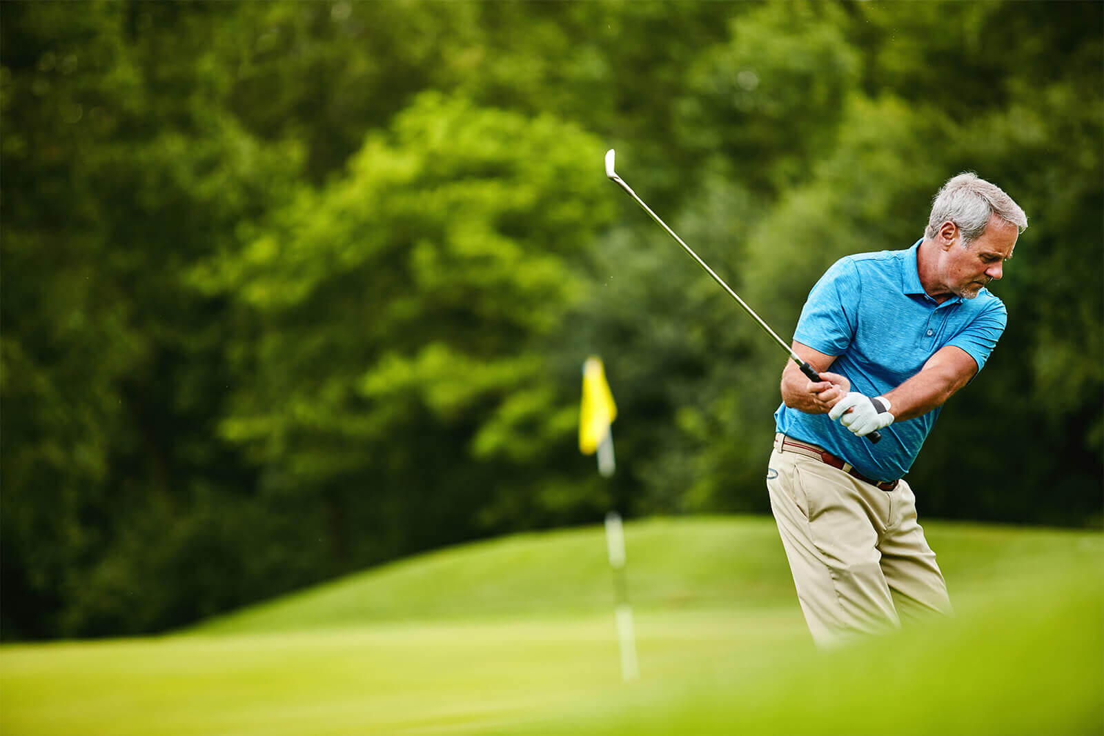 Older man swinging golf club on green course