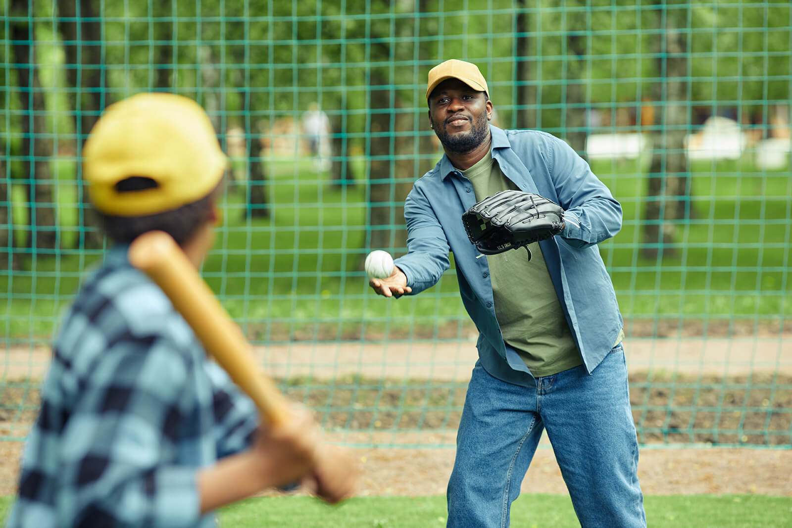 Man pitching a baseball to a child holding a bat in a park