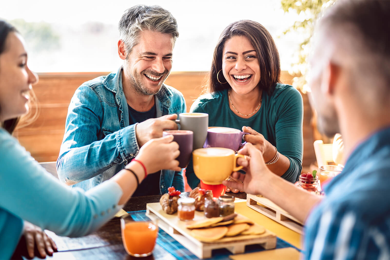 Group of friends laughing and toasting with coffee at breakfast