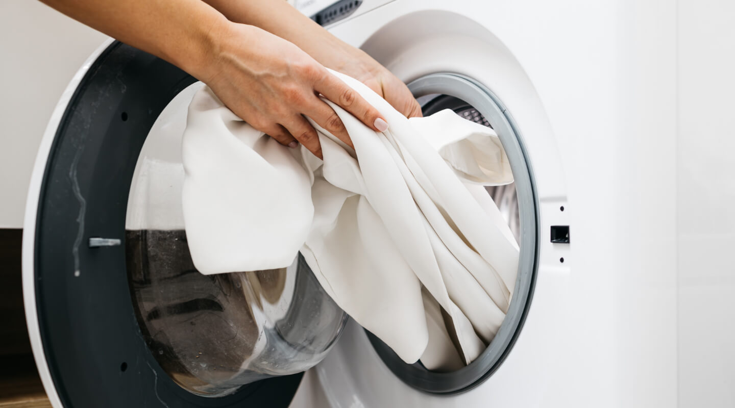 Hands loading white laundry into a front-load washing machine