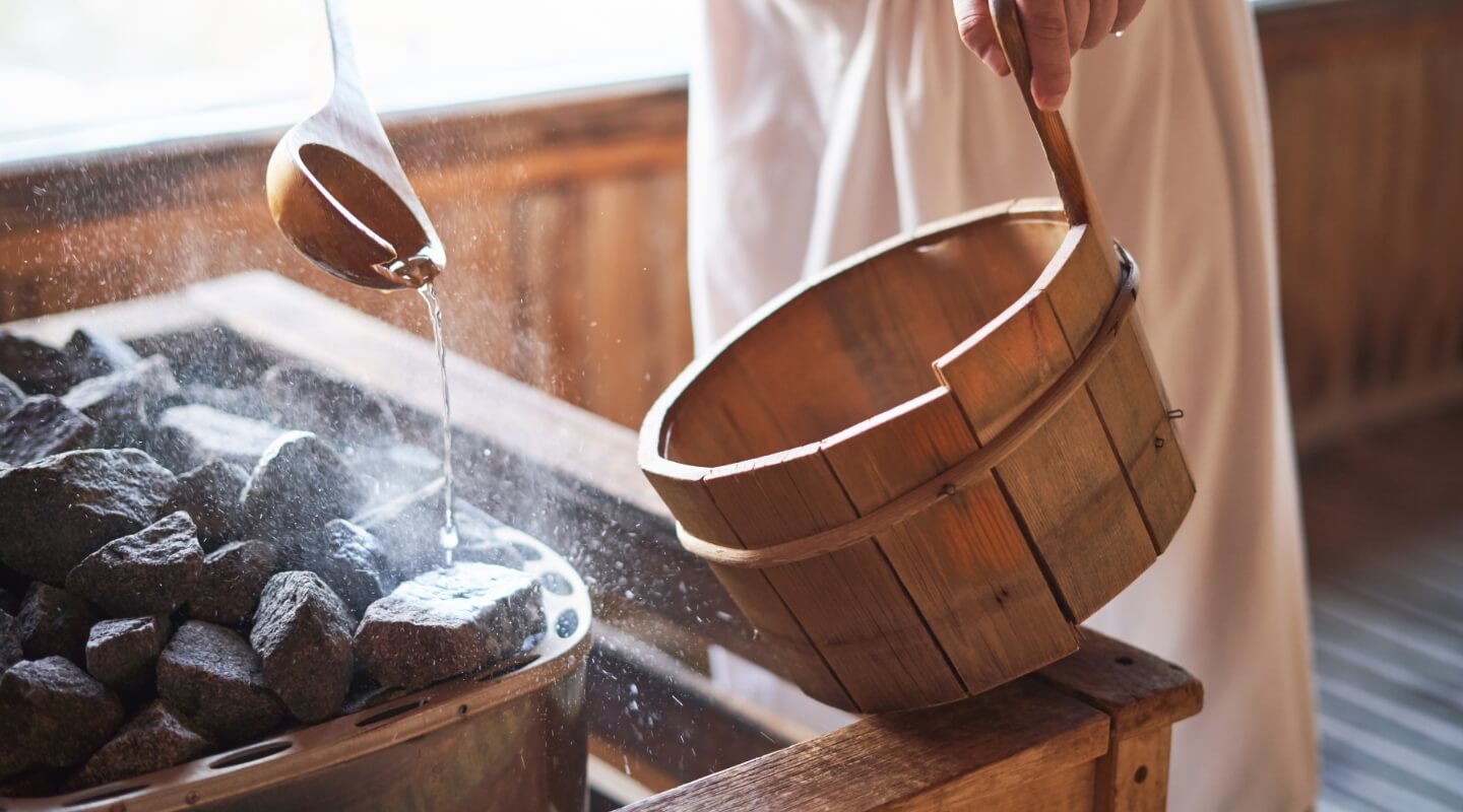 Pouring water from a wooden ladle onto hot sauna stones for steam