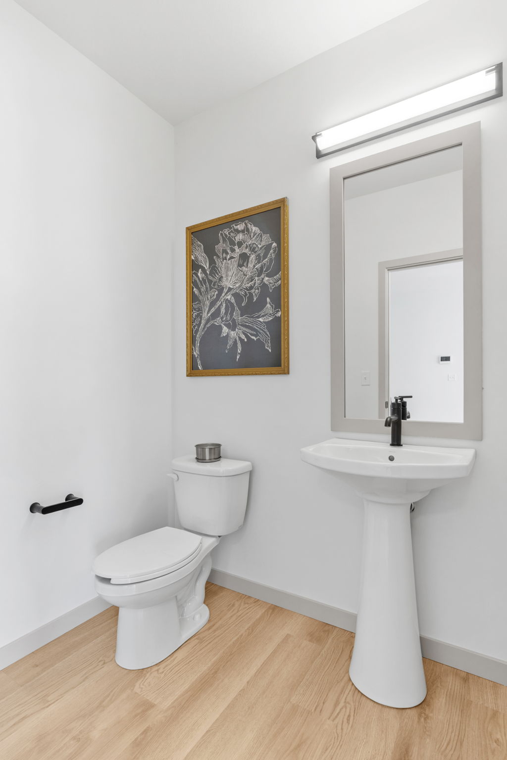 Bright half bathroom with white pedestal sink, large mirror, and wood-style flooring