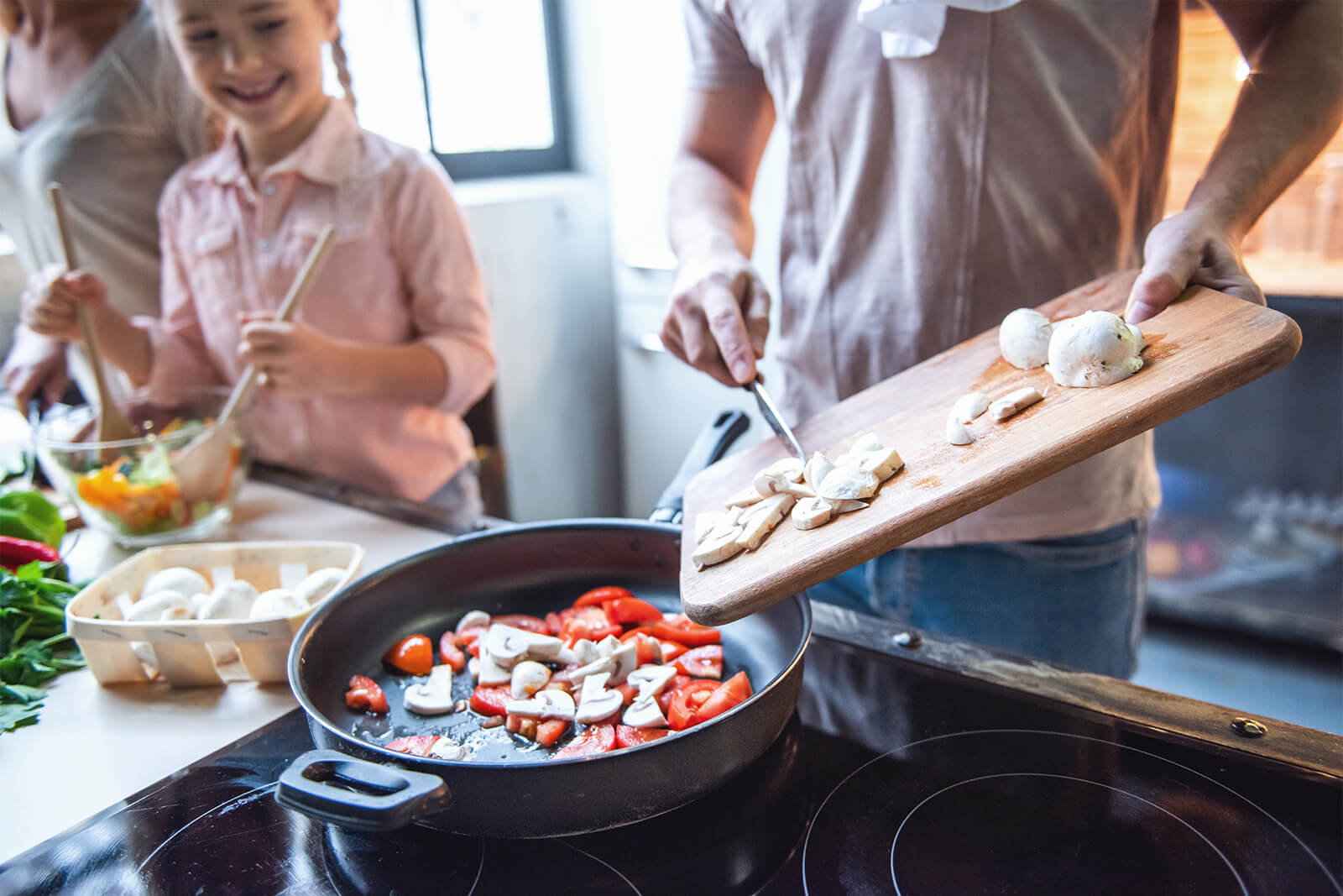 Family cooking together, slicing mushrooms and vegetables in kitchen