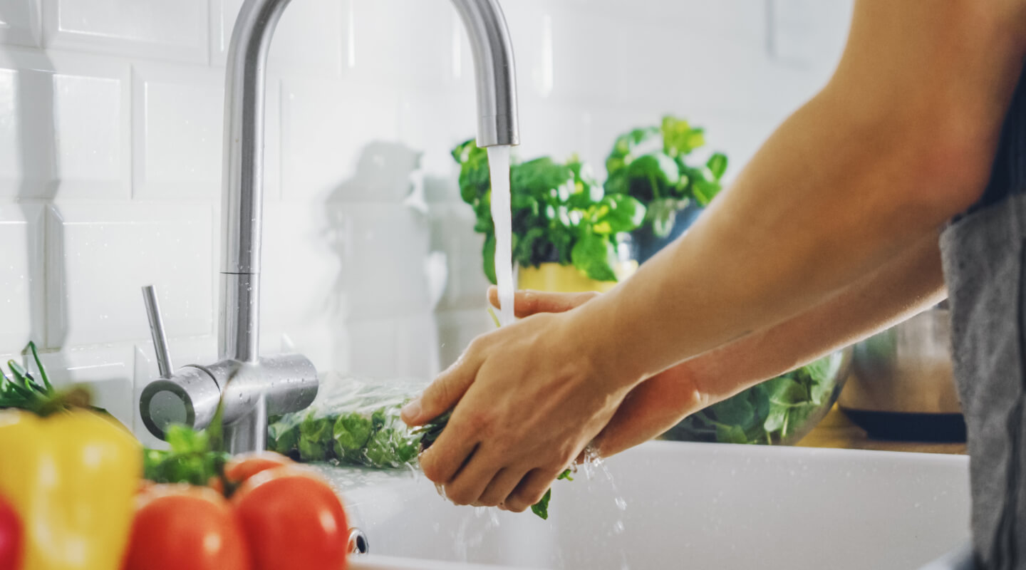Person rinsing leafy greens under a kitchen faucet
