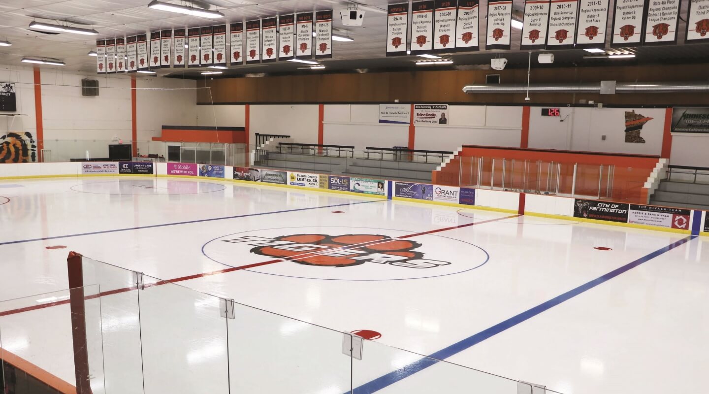 Indoor ice arena with team banners hanging from the rafters and a tiger logo at center ice.
