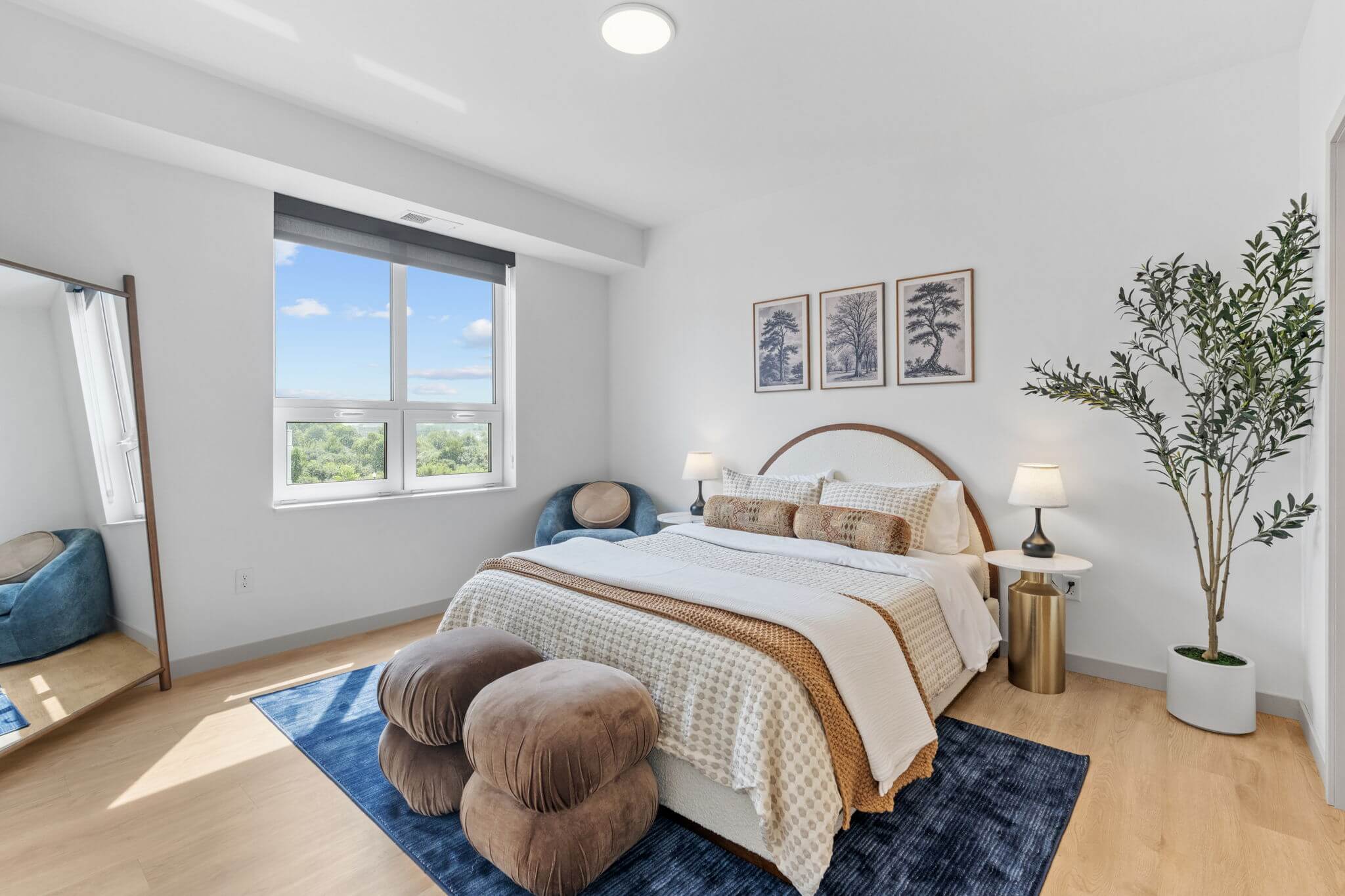 Bedroom with large window, round headboard, and neutral-toned bedding at Rye Apartments